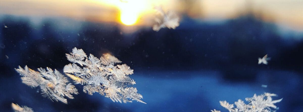 Schneeflocken vor blauem Hintergrund, am Hoizont scheint die Sonne